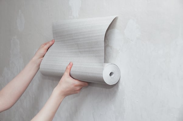 roll of gray wallpaper in the hands of a Caucasian woman. Attaches wallpaper to the wall.